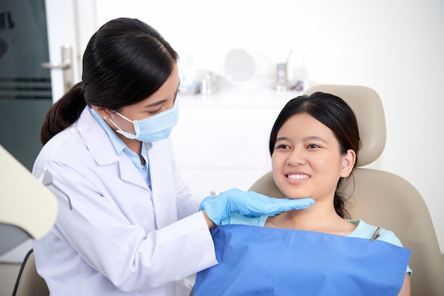 Азиатский женский дантист проверяя зубы пациента, и женщина улыбается