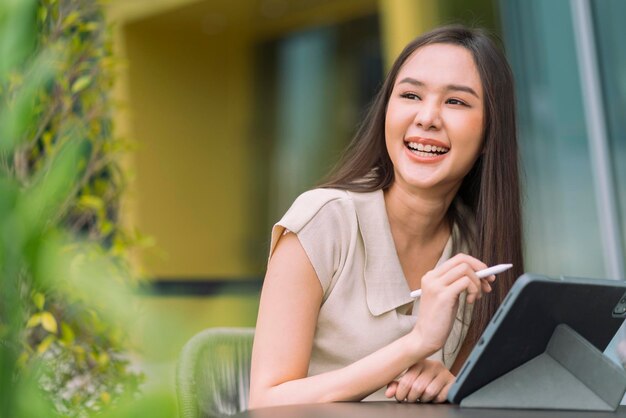 아시아 여성 디지털 유목민 행복 자유 쾌활한 미소 정원 야외에서 태블릿을 사용하여 작업