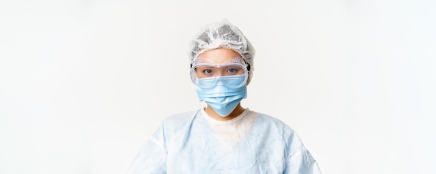 흰색 배경 위에 얼굴 의료 마스크와 보호 안경이 서 있는 개인 보호 장비를 착용한 아시아 여성 의사 또는 간호사