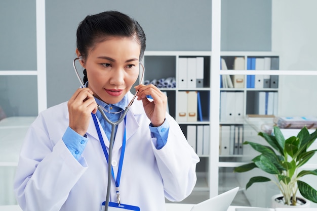Asian female doctor putting on stethoscope at work