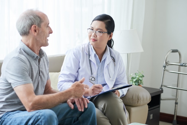 Asian female doctor talking to senior Caucasian patient during house call