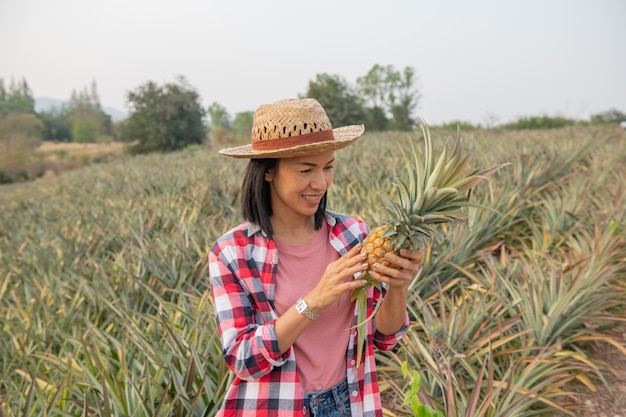 アジアの女性農民は農場でパイナップルの成長を見ます、若いきれいな農夫の女性は農地に立っています。