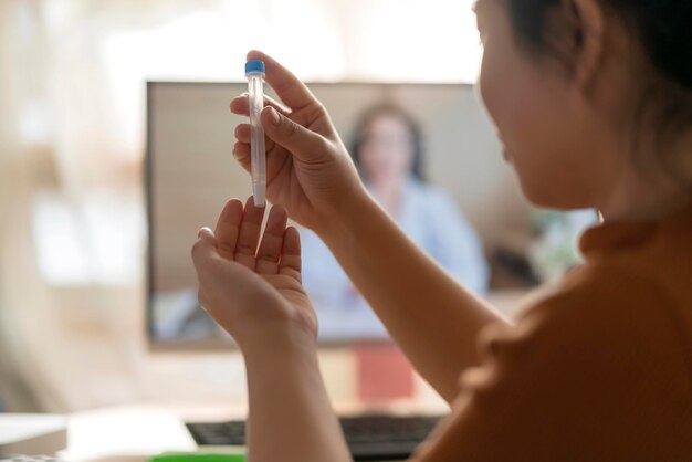 アジアの女性の手の鼻腔スワブは、自宅での遠隔ビデオ医師の指導によるSARSco2ウイルスの検出のために自分で迅速なテストをテストします隔離検疫の概念