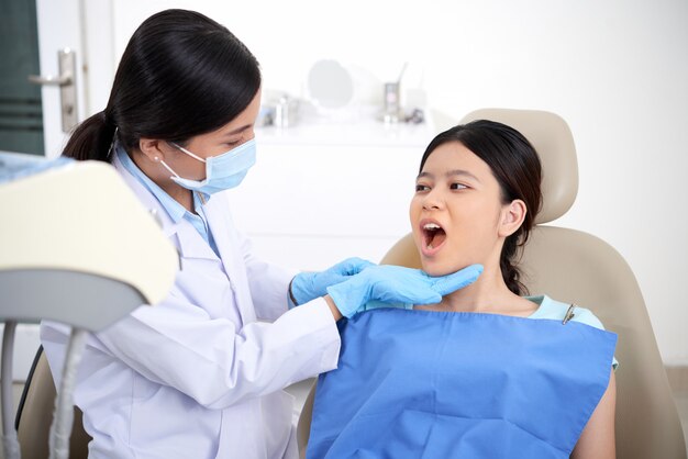 Free photo asian female patient sitting in chair with open mouth, and dentist looking at her teeth