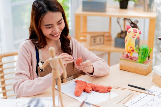 Asian Female spend weekend day for her hobby clay scuplture online course at home young adult making study from tablet streaming course online in apron costumeasian casual lifestyle at home