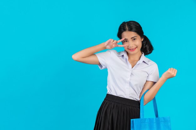 Азиатская студентка, которая крутит сумку из ткани и показывает различные жесты на синем фоне.
