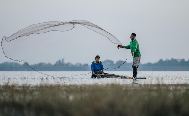アジアの漁師と友人は早朝に川で釣りにボートと漁網を使用し、スペースをコピーします