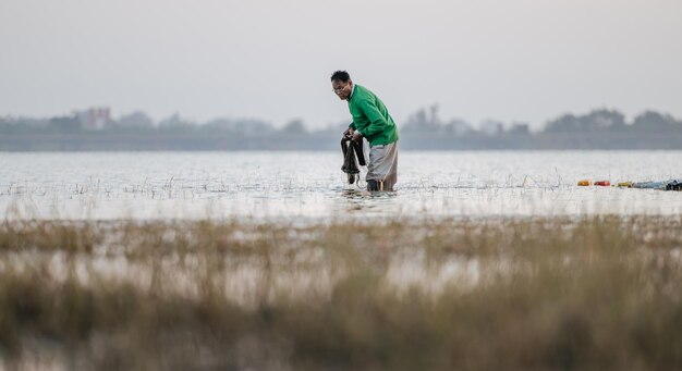 早朝に水と漁網に立って川で釣りをするアジアの漁師、コピースペース