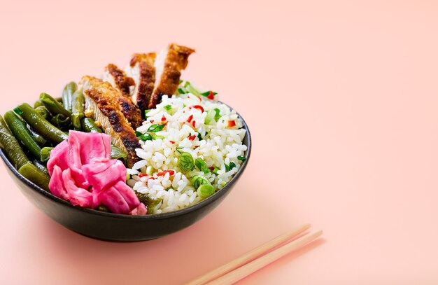 Asian food idea. Rice with spices and turkey wedges in a black bowl with sauteed green beans, hot peppers, fermented cabbage. Close-up with copy space