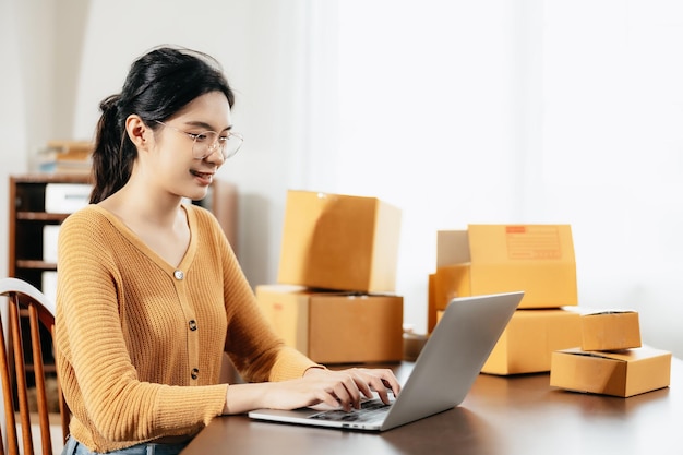 Asian freelance woman using laptop for checking customer order online shipping boxes at home