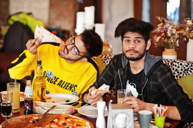 Asian friends guys eating pizza during party at pizzeria Happy indian people having fun together eating italian food and sitting on couch