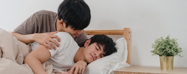 Asian Gay couple kiss and hug on bed at home. Young Asian LGBTQ men happy relax rest together spend romantic time after wake up in bedroom at home in the morning .