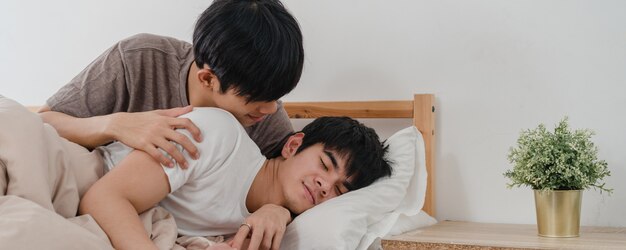 Asian Gay couple kiss and hug on bed at home. Young Asian LGBTQ men happy relax rest together spend romantic time after wake up in bedroom at home in the morning .