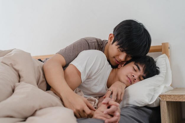 Asian Gay couple kiss and hug on bed at home. Young Asian LGBTQ men happy relax rest together spend romantic time after wake up in bedroom at home in the morning .