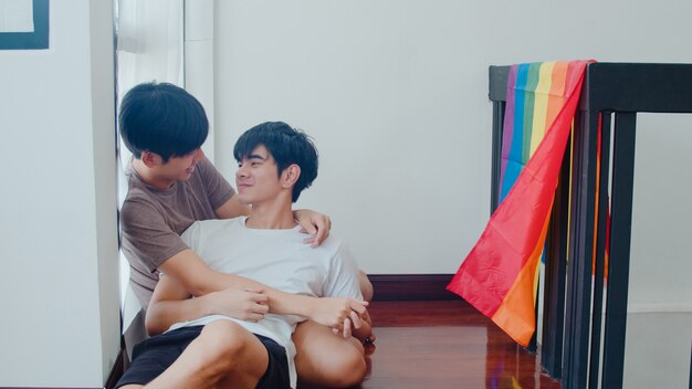 거짓말을 하 고 집에서 바닥에 포옹 아시아 게이 커플. 행복 키스 젊은 아시아 LGBTQ + 남자는 아침에 현대 집에서 무지개 깃발로 거실에서 낭만적 인 시간을 보내십시오.