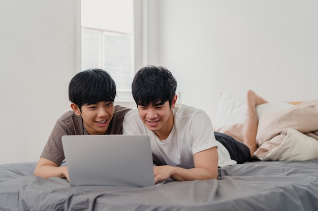 Азиатские гомосексуалисты lgbtq соединяют использование компьтер-книжки компьютера на современном доме. Молодой любитель Азии мужчина счастлив расслабиться отдохнуть вместе после пробуждения, смотреть фильм, лежа на кровати в спальне у себя дома в первой половине дня.