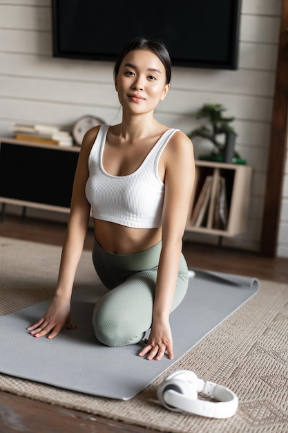 Asian girl doing yoga stretching at home workout in her living room wearing activewear