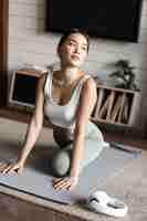 Free photo asian girl doing yoga stretching at home workout in her living room wearing activewear