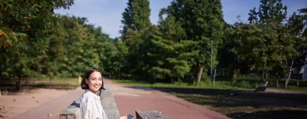Бесплатное фото Азиатская девушка рисует в парке, сидя на улице в солнечный день с помощью цифрового графического планшета и ручки