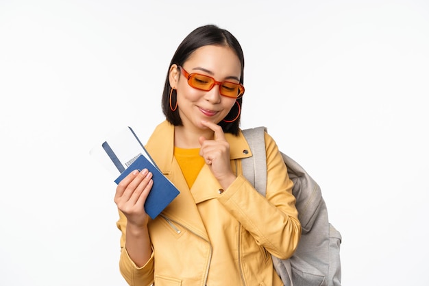 Asian girl tourist with boarding tickets and passport going abroad holding backpack thinking of travelling standing over white background
