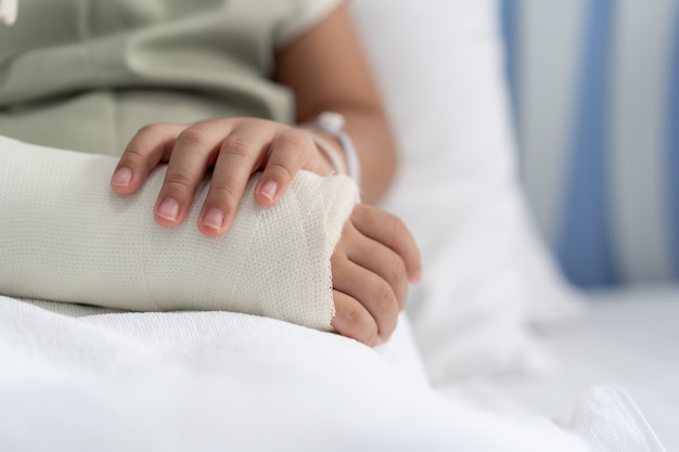 Лечение азиатской девушки в больнице, лежащей на кровати, больно сломанной рукой после операции.