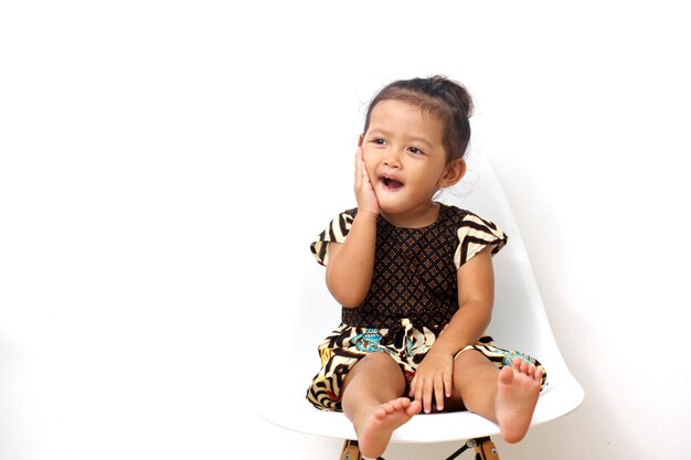 Asian girl wearing batik clothes is sitting on chairs while hold her cheek