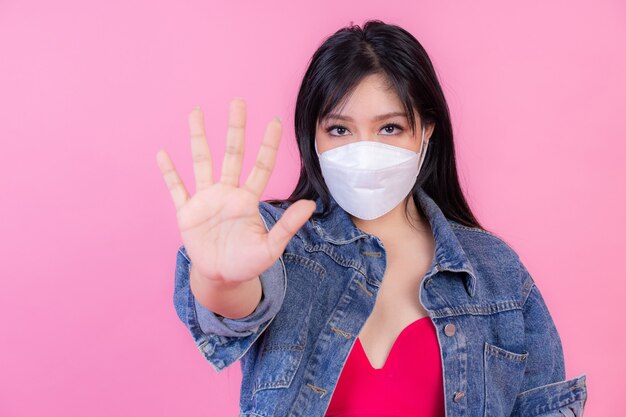 Азиатская девушка в маске для лица показывает жест рукой, чтобы остановить вспышку вируса короны, защитить распространение Covid-19