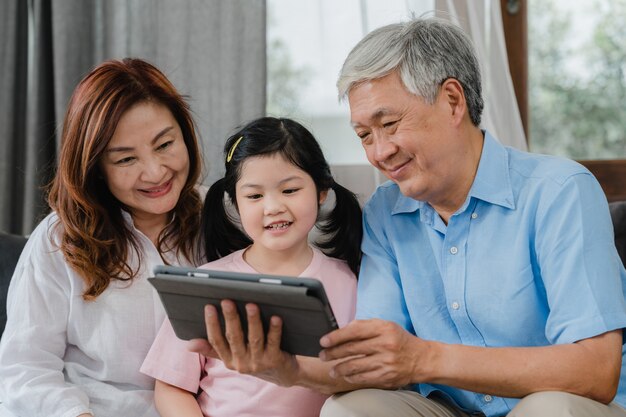 Азиатские бабушки и дедушки и видео внучки дома. Старший китаец, дедушка и бабушка довольны девушкой, с помощью мобильного телефона, видео звонок, разговаривая с папой и мамой, лежа в гостиной дома.