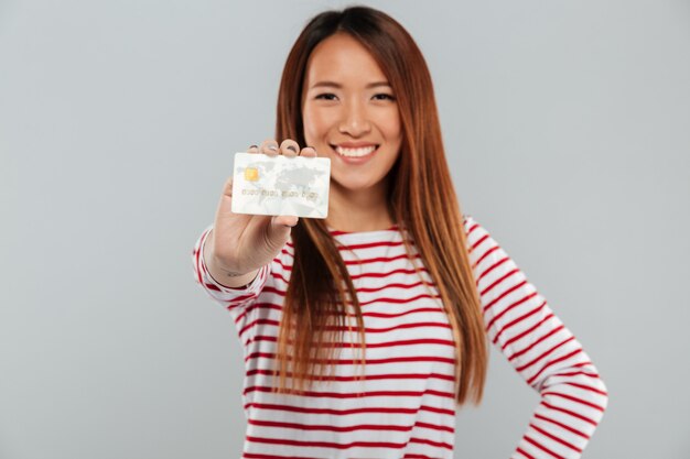 Asian happy lady standing isolated holding credit card.