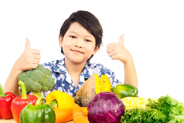 アジアの健康的な少年の様々な新鮮なカラフルな野菜と幸せな表情を示す