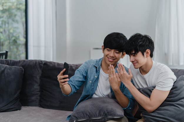 Asian influencer Gay couple vlog at home. Asian LGBTQ men happy relax fun using technology mobile phone record lifestyle vlog video upload in social media while lying sofa in living room .