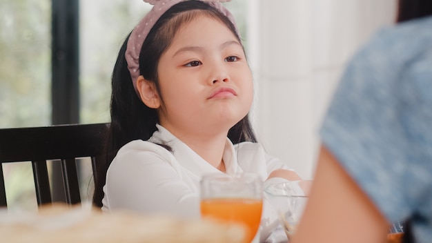 Asian Japanese daughter bored with food. Lifestyle kids sad dislike food upset breakfast meal in modern kitchen at house in the morning .