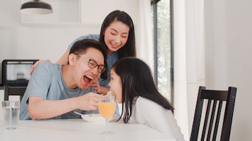 Asian japanese family has breakfast at home. asian happy dad, mom, and daughter eat spaghetti drink orange juice on table in modern kitchen at house in the morning .