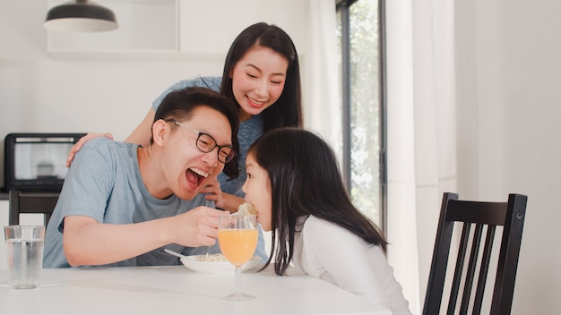 アジア系の日本人家族は家で朝食をとります。アジアの幸せなお父さん、お母さん、娘は、朝の家のモダンなキッチンのテーブルでスパゲッティドリンクオレンジジュースを食べます。
