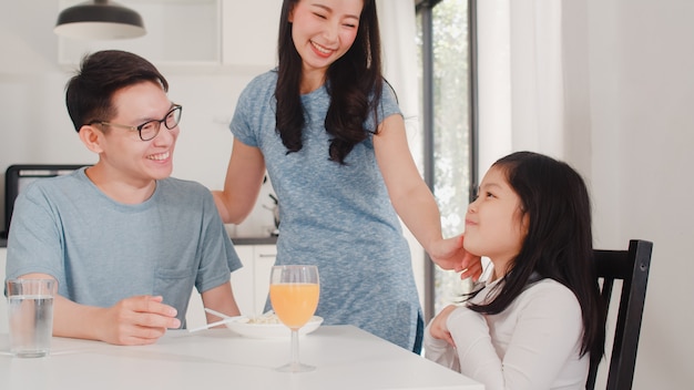 アジア系の日本人家族は家で朝食をとります。アジアの幸せなお父さん、お母さん、娘は、朝の家のモダンなキッチンのテーブルでスパゲッティドリンクオレンジジュースを食べます。