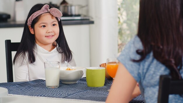 Asian Japanese family has breakfast at home. Asian mom, dad, and daughter feeling happy talking together while eat bread, corn flakes cereal and milk in bowl on table in the kitchen in the morning.