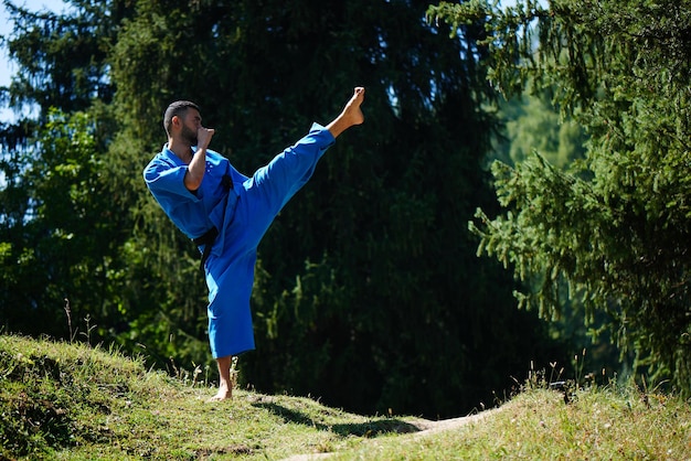 아시아 카자흐 가라데 파이터는 복사 공간이 있는 여름의 아름다운 자연 경관에서 파란색 기모노 유니폼을 입고 전투를 벌이고 있습니다.