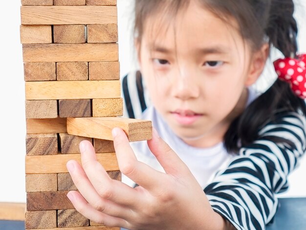 Asian kid is playing jenga, a wood blocks tower game for practicing physical and mental skill