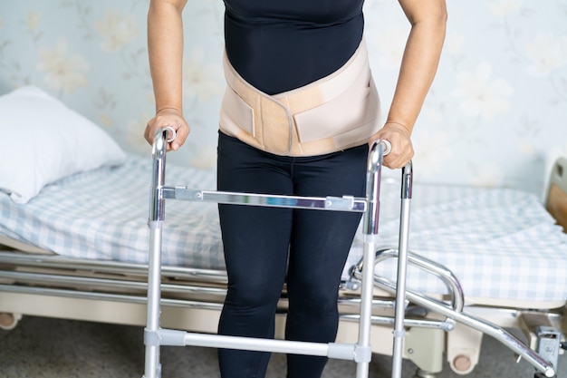 Азиатская женщина-пациентка носит пояс для поддержки боли в спине для ортопедического поясничного отдела с ходунками.