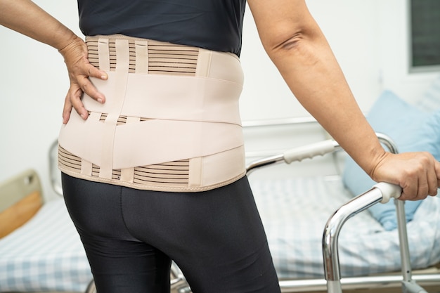 Азиатская женщина-пациентка носит пояс для поддержки боли в спине для ортопедического поясничного отдела с ходунками.