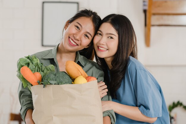 Asian Lesbian lgbtq women couple hold grocery shopping paper bags at home