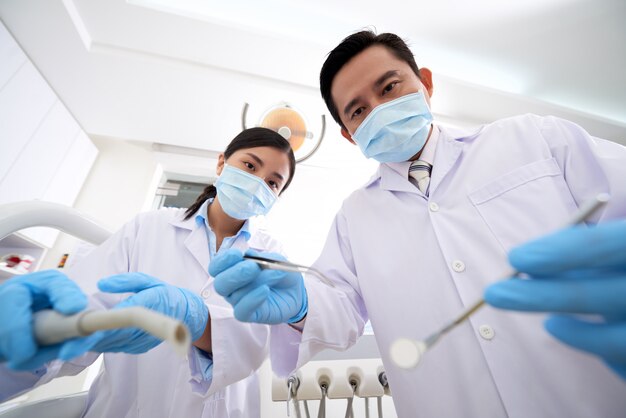 Азиатские мужчины стоматолог и медсестра, стоя над и держа инструменты для стоматологического осмотра