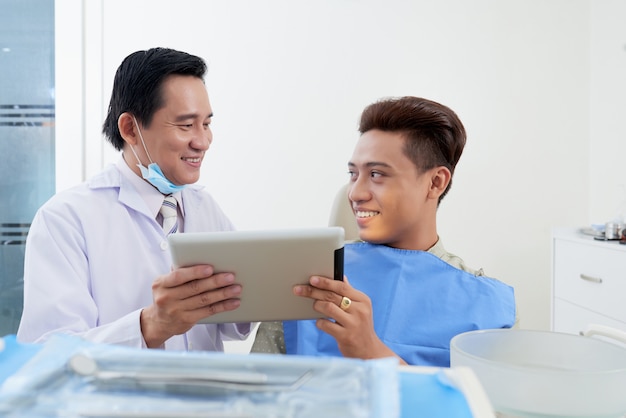 Азиатский мужской дантист с таблеткой советуя с пациентом в клинике