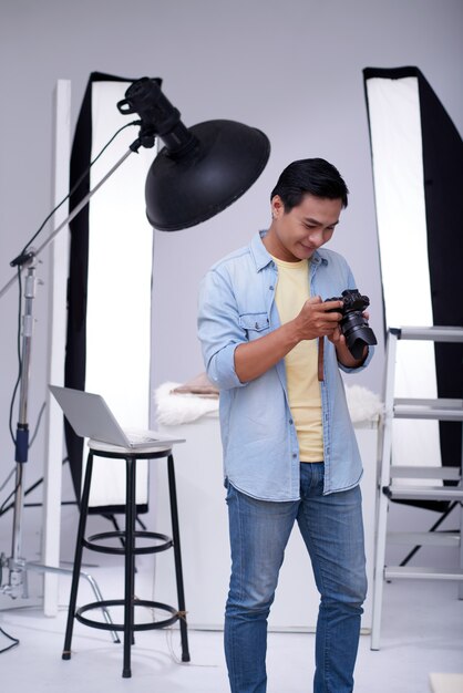 Asian male fashion photographer checking photos on camera in studio