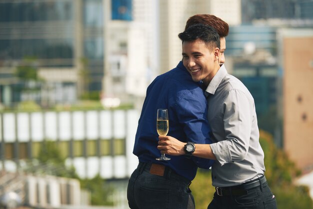 Asian male friends hugging at urban rooftop champagne party