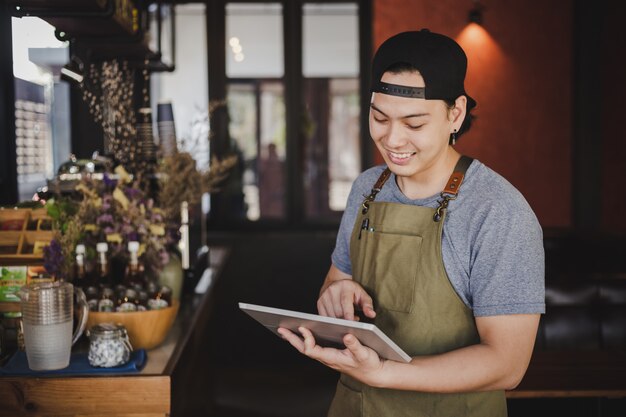 アジア人男性バリスタコーヒーカフェで顧客からの注文を確認するためのタブレットを保持しています。