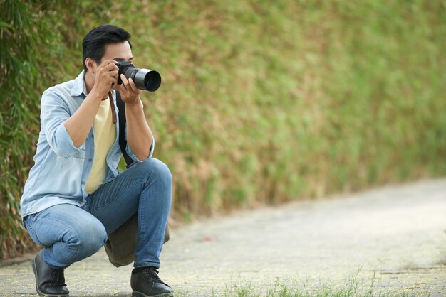 アジア人の男性が公園でしゃがみ込んで、デジタルカメラで写真を撮る