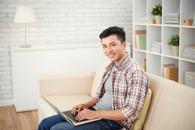 Азиатский мужчина делает внештатную работу на ноутбуке Siiting на диване у себя дома