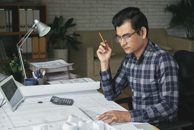 Asian man drawing blueprint in his cozy office