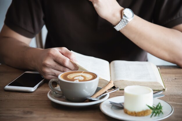 アジア人の男性がコーヒーを飲むと本を読んで